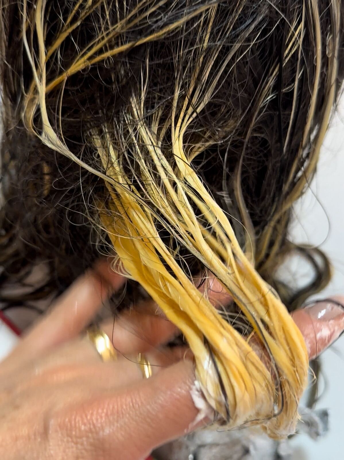 Mechas de cabelo clareadas com fundo alaranjado e amarelo visível, sendo avaliadas antes da aplicação do tonalizante