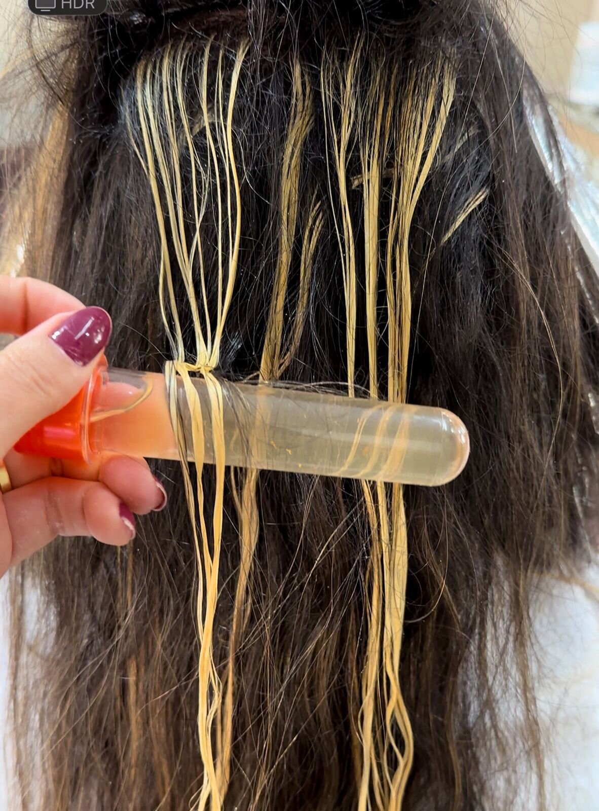Mecha de cabelo sendo testada com tubo de ensaio durante processo de coloração, mostrando a leitura do fio antes de decidir a fórmula